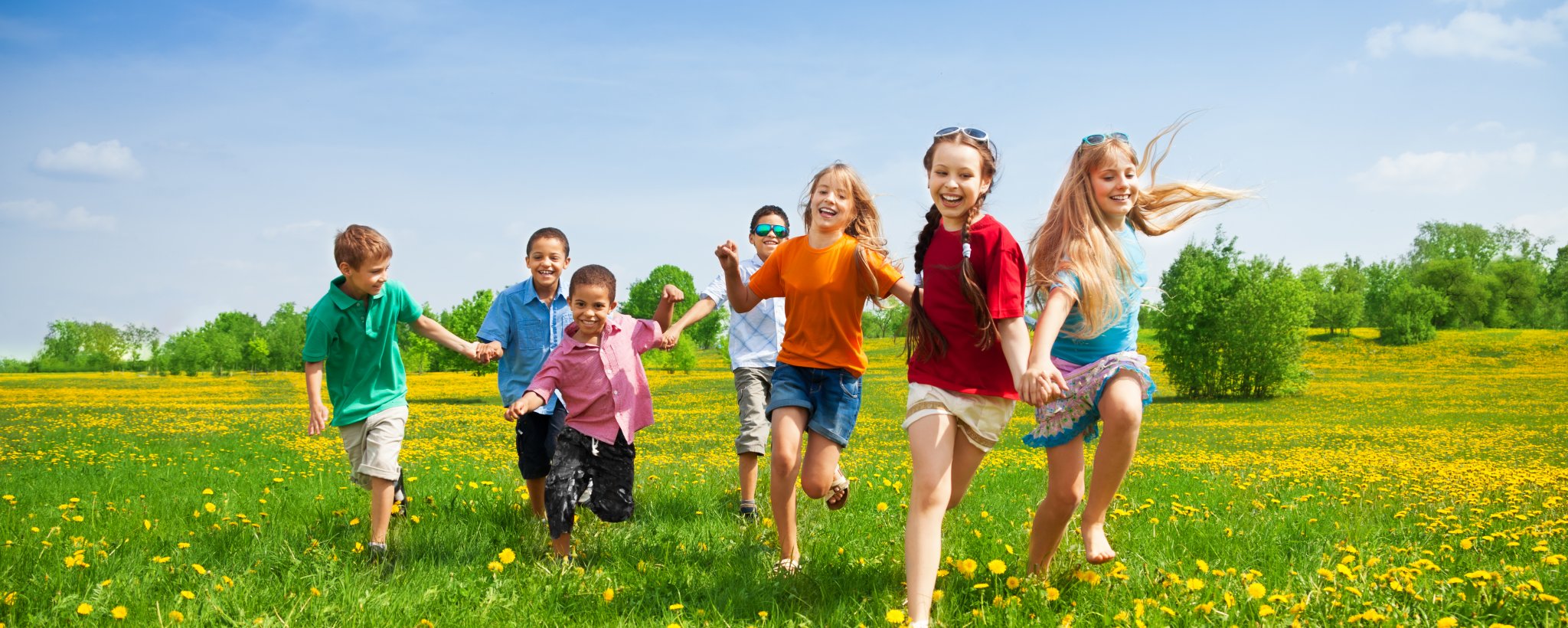 Diverse group of children running in green meadow with yellow flowers